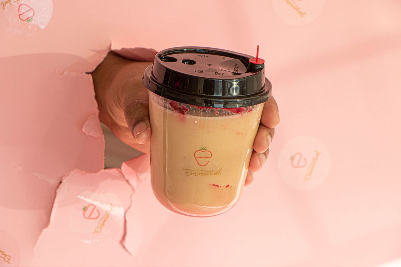 Close-up of hand holding bubble tea cup through torn pink paper background.